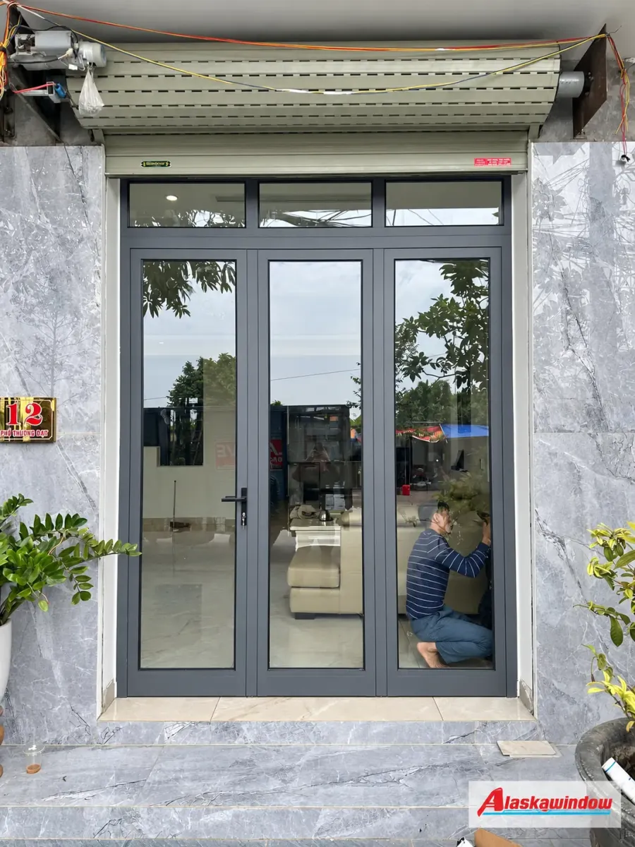 Bộ cửa nhôm kính xám ghi với các ô kính phía trên tại mặt tiền nhà ở Tam Bình