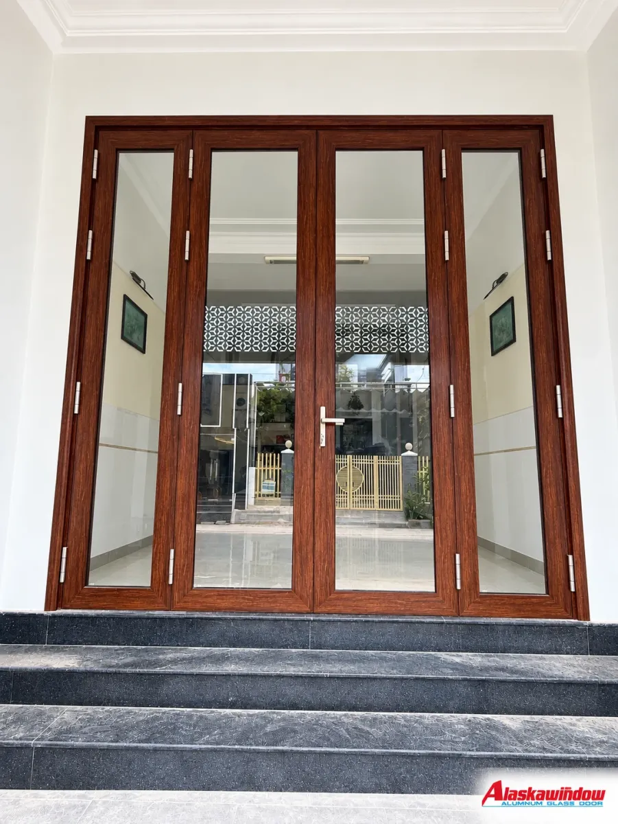 Bộ cửa kính nhiều cánh tông nâu đặt trên bậc đá trước nhà Bộ cửa kính nhiều cánh tông nâu đặt trên bậc đá trước nhà