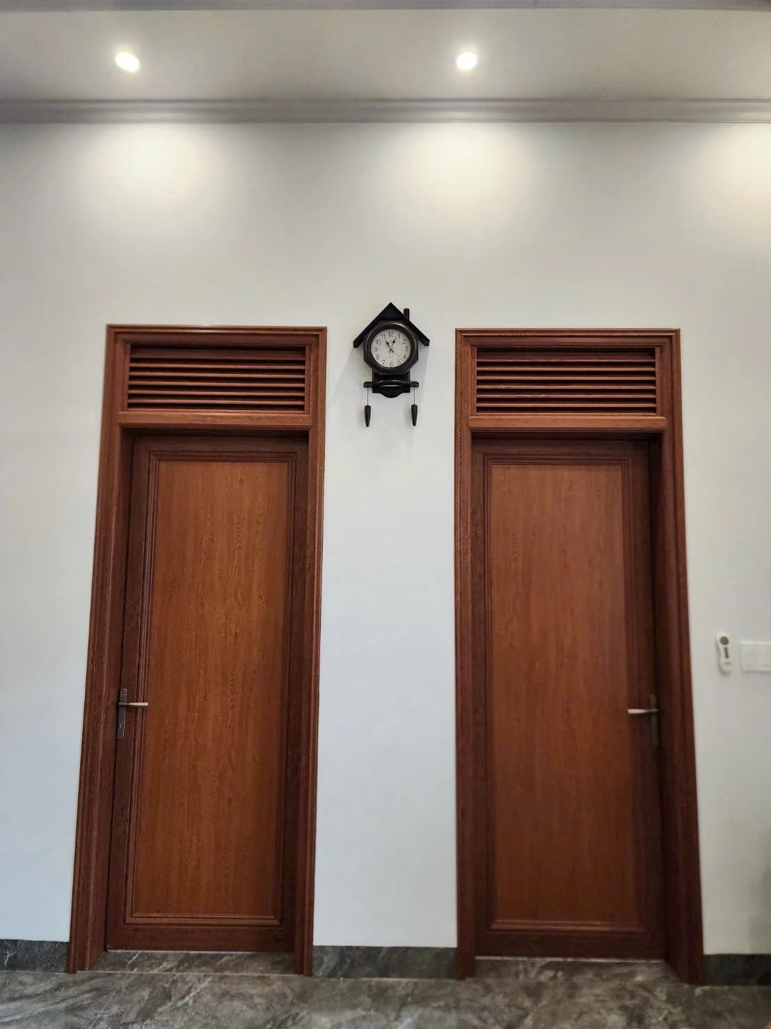Hai bộ cửa pano màu vân gỗ với ô lá sách trên cùng mảng tường